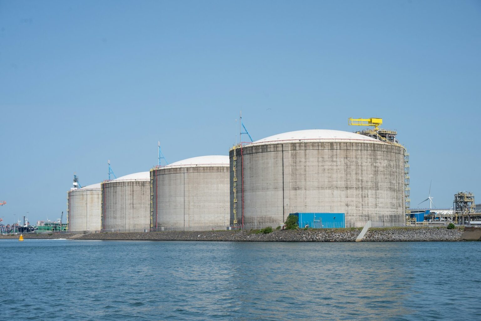 Industrial storage tanks beside a port under a clear sky